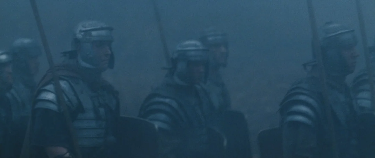 Centurion (2010) movie still: medium — A group of Roman soldiers in traditional armor stands together amidst heavy morning fog. The soldiers hold…