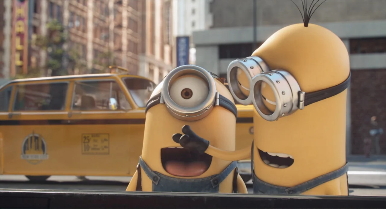 Minions (2015) movie still: medium — A city street features a yellow taxi parked in front of brick urban buildings. Two yellow minions stand in the…
