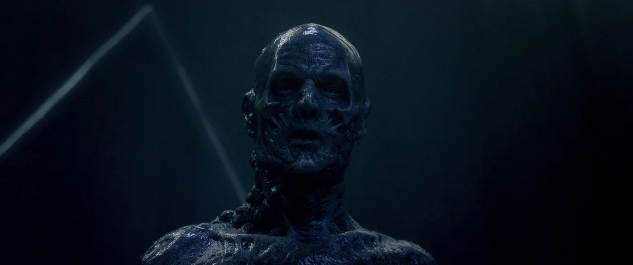 The Void (2016) movie still: closeup — A dark, nondescript void surrounds the figure, with thin white light streaks in the background. A humanoid…