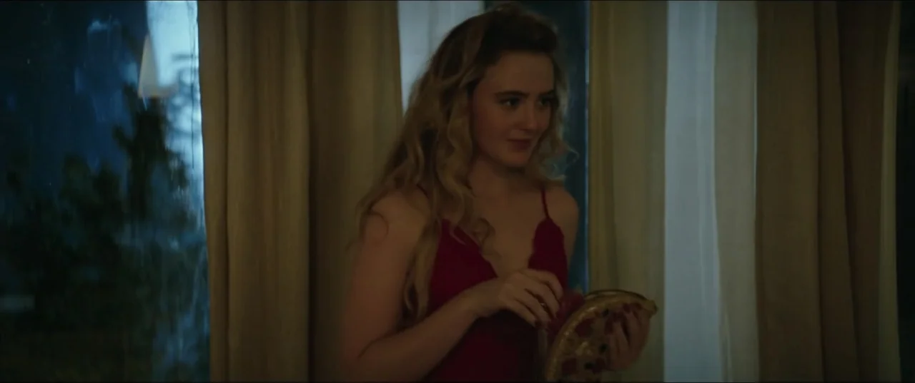 Blockers (2018) movie still: medium — A dimly lit room features heavy floor-length gold curtains and a window. A young woman with blonde hair stands…
