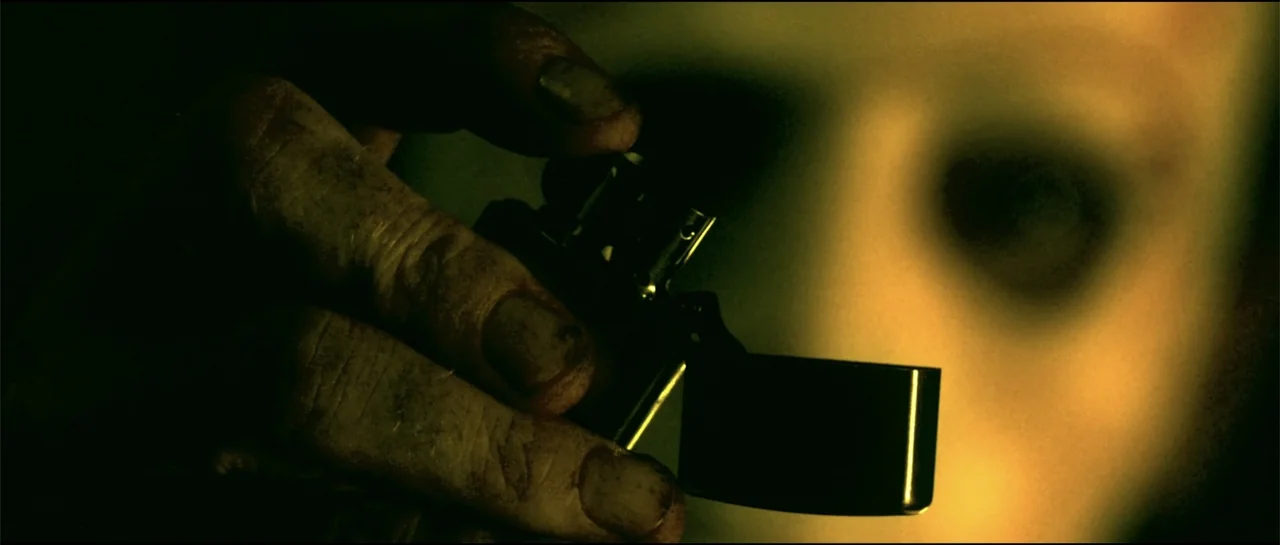 The Vault (2017) movie still: closeup — A dark indoor space is illuminated by the flicker of a metallic lighter. A person's soiled hand holds the…