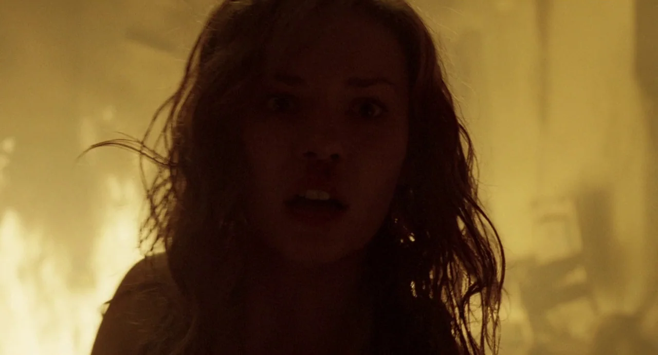 House of Wax (2005) movie still: closeup — An interior space is filled with diffuse orange light from an off-screen fire. A young woman looks…