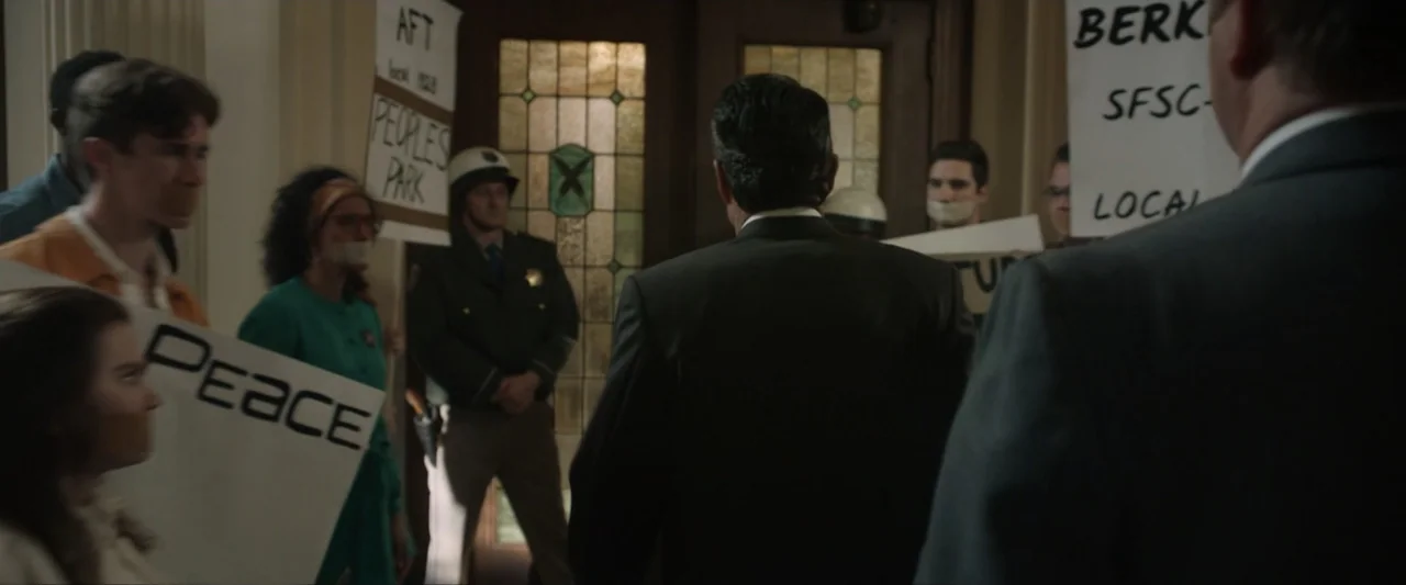 Reagan (2024) movie still: medium — A stone-floored entryway features a large wood-framed glass door with decorative textured panels. A man in a…