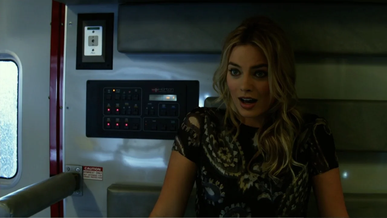 Focus (2015) movie still: medium — An ambulance interior features sterile grey walls with a control panel and window. A young woman with blonde hair…
