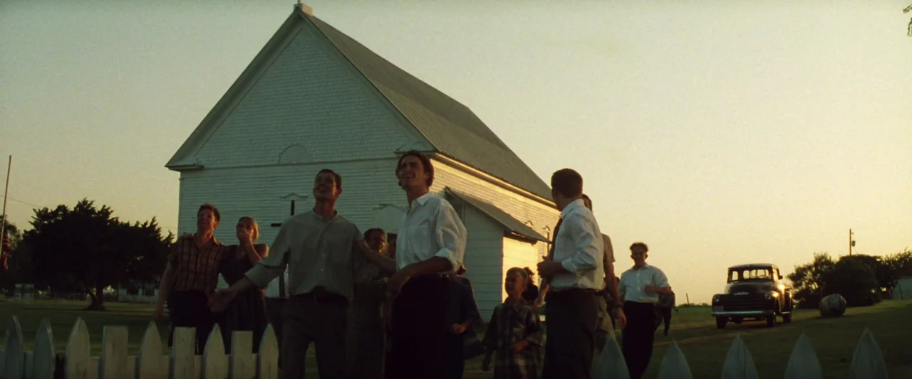 Armageddon (1998) movie still: wide — A group of people gathers in front of a white wooden church at dusk. The individuals look toward the sky while…