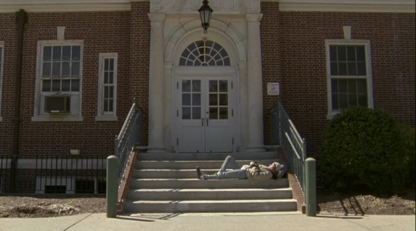 The House Of The Devil (2009) movie still: wide — A brick building with white trim and large double doors features wide concrete steps. A person…
