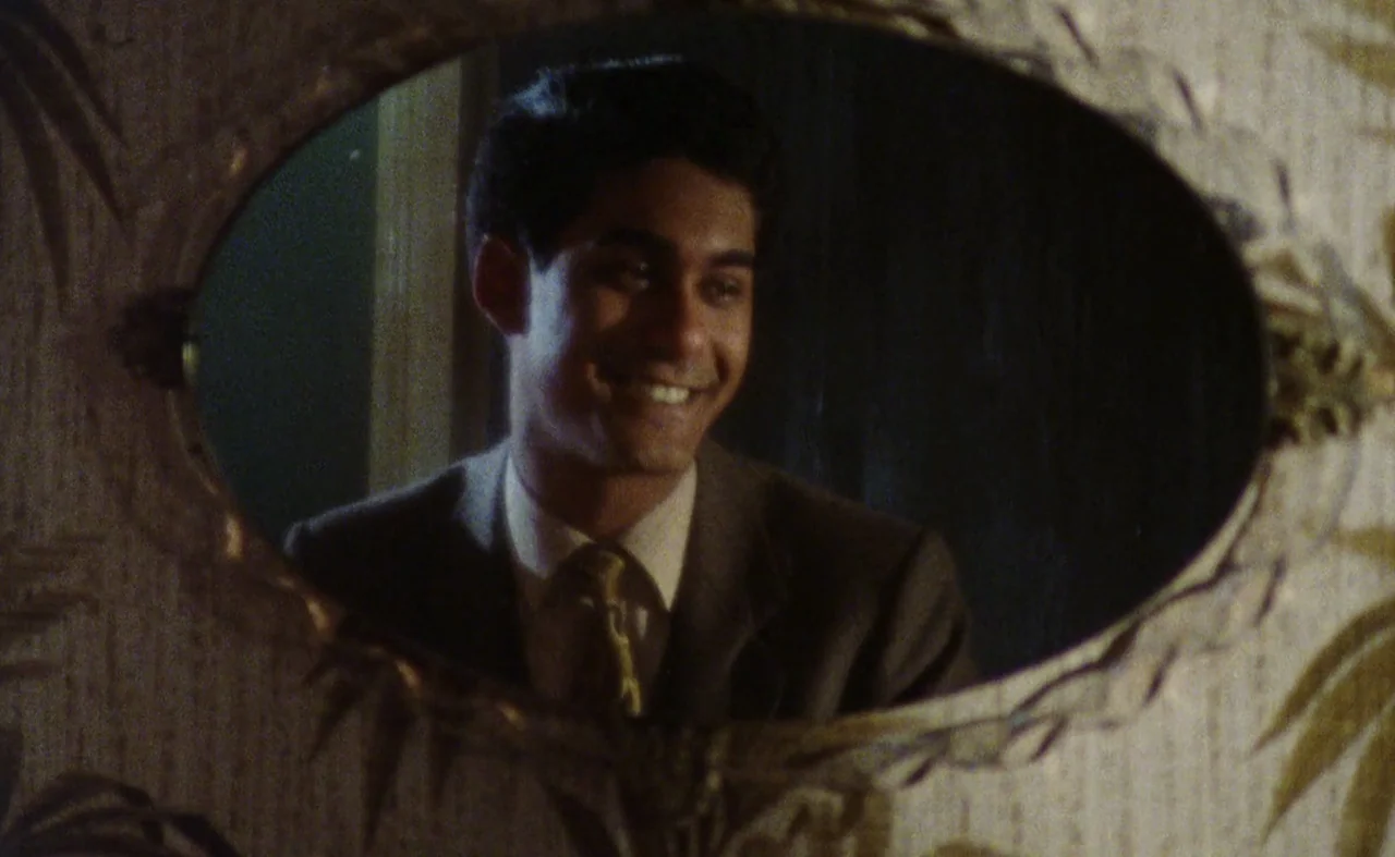 My Beautiful Laundrette (1985) movie still: closeup — A man looks into a small, oval, ornately framed mirror mounted on a wall. His reflection…