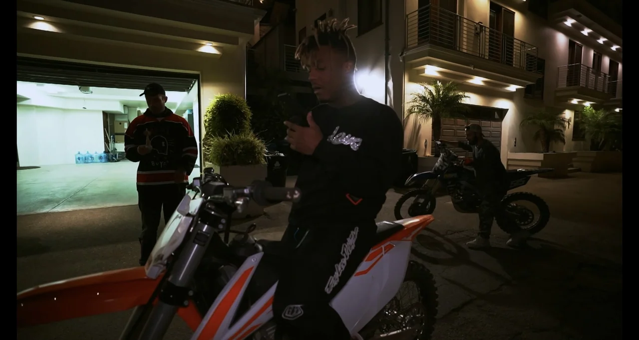 Juice WRLD: Into the Abyss (2021) movie still: medium — A modern multi-story residential building with a lighted garage at night. A young man sits…