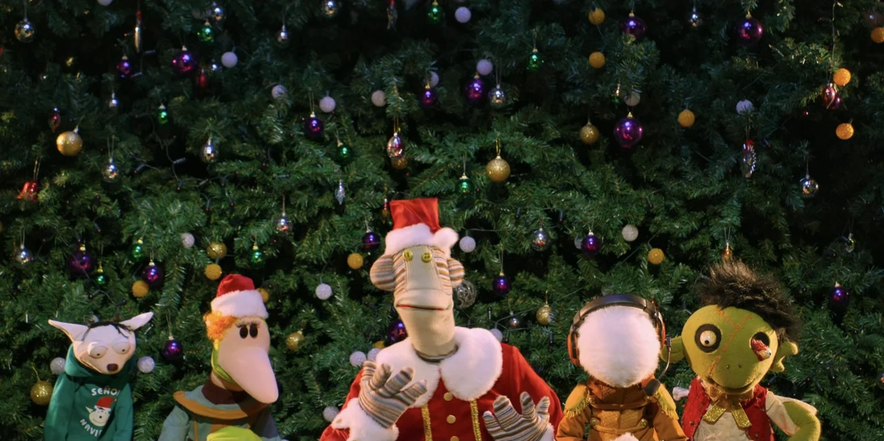 31 Minutes: One Hot Christmas (2025) movie still: medium — A decorated Christmas tree filled with colorful ornaments serves as a festive background.…