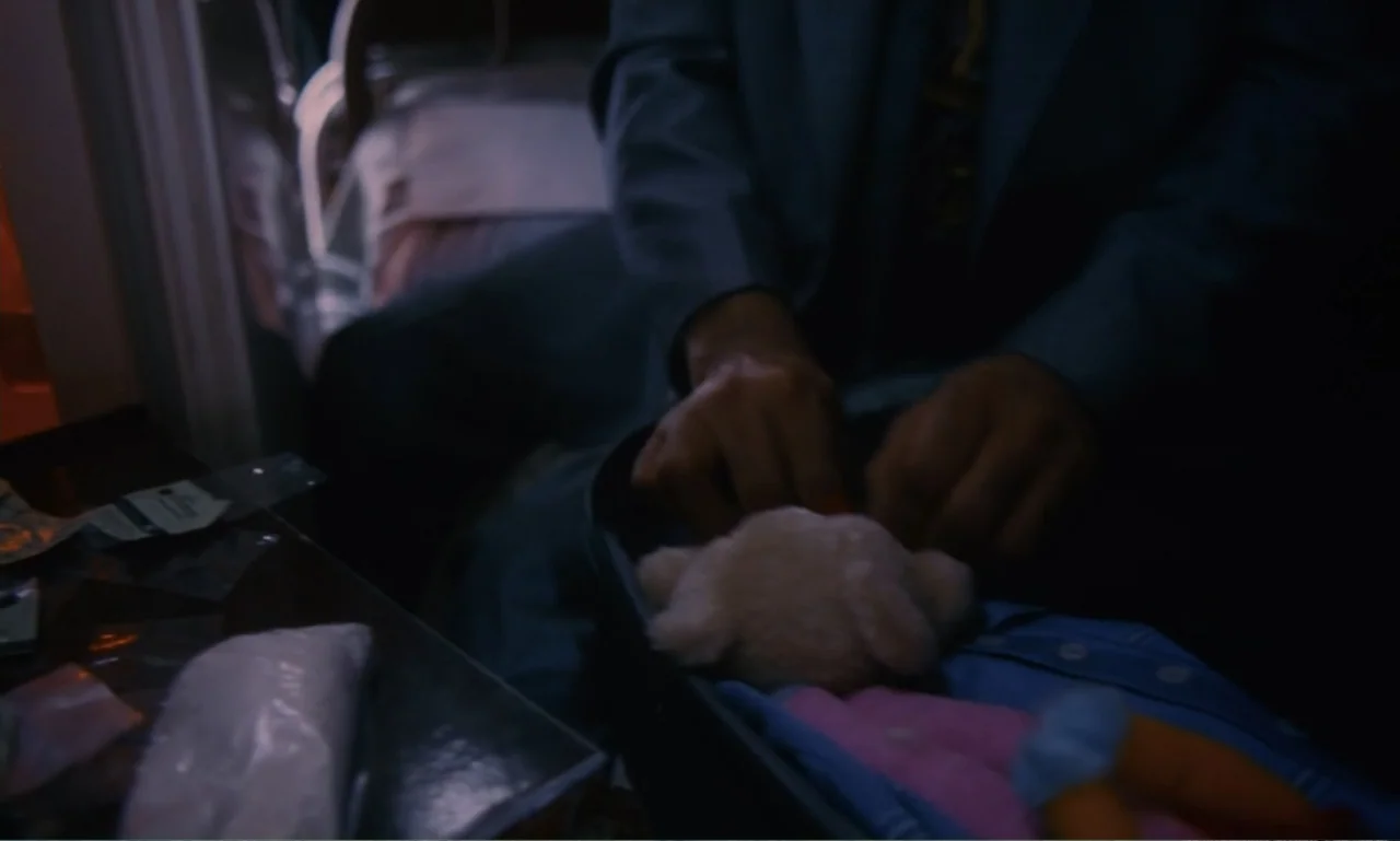 Chungking Express (1994) movie still: medium — A dimly lit interior space with shadows cast across a bed and suitcase. A person is placing a stuffed…