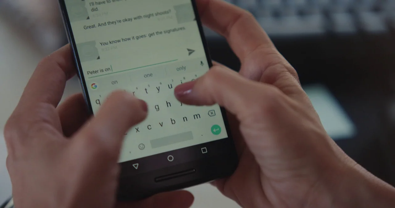Violet (2021) (2021) movie still: closeup — A close-up shot of hands typing a text message on a modern smartphone screen. The soft focus background…