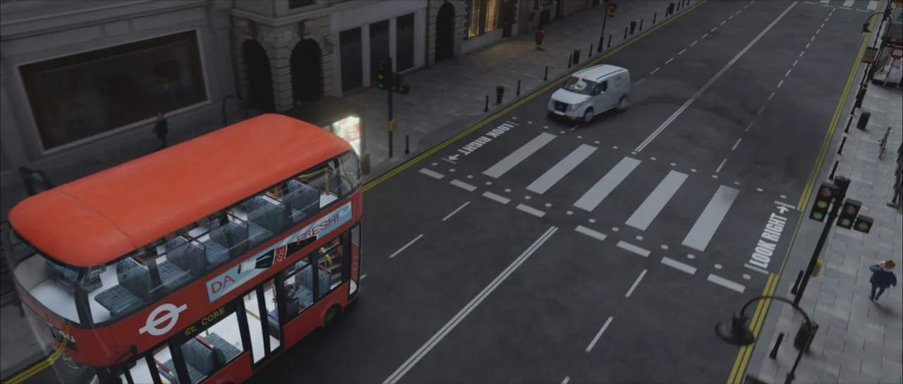 Mummies (2023) movie still: wide — A high-angle view of a city street featuring a red double-decker bus. The bus moves past a pedestrian crosswalk…