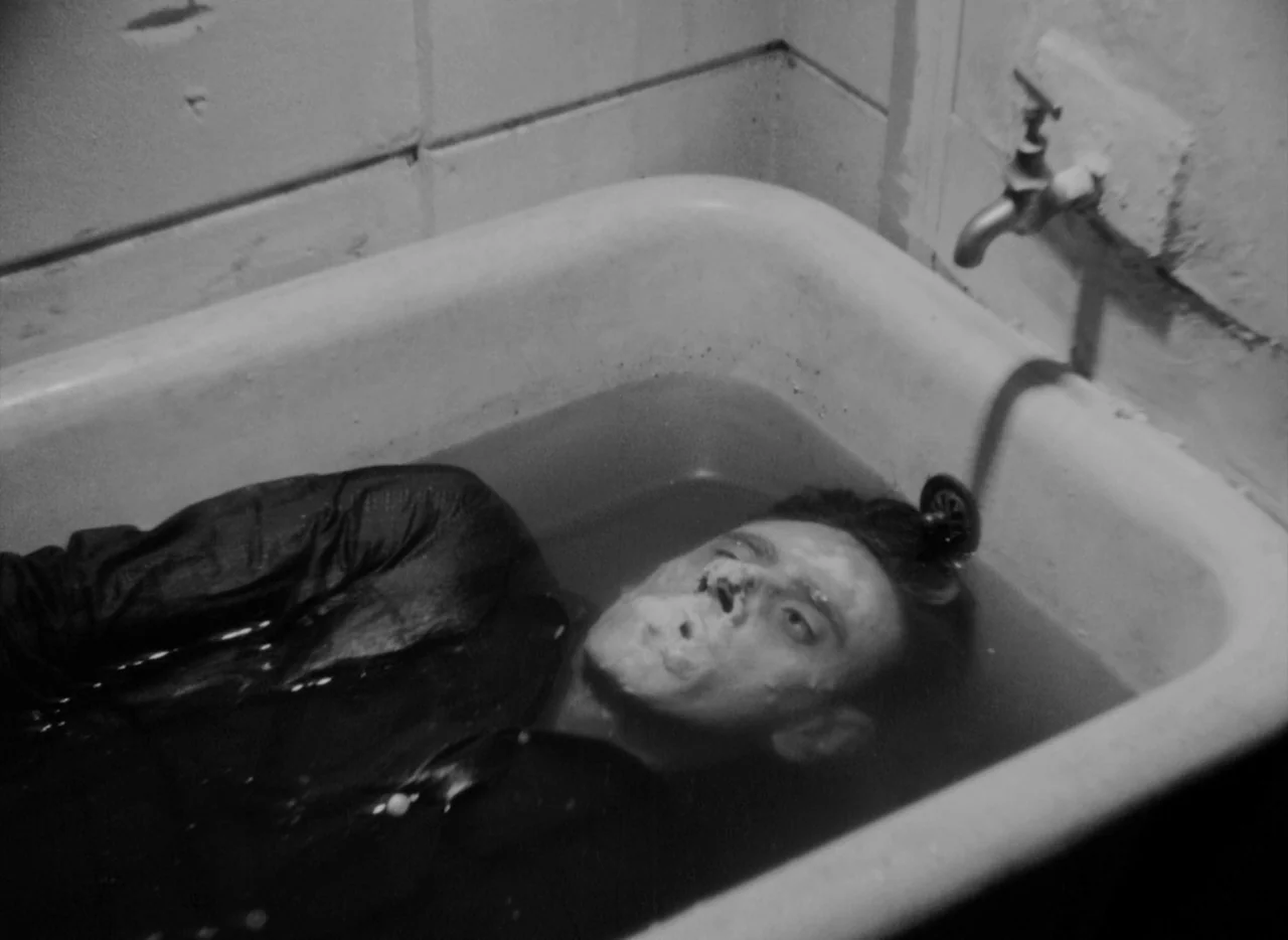 At Midnight I’ll Take Your Soul (1964) movie still: medium — A man lies inside a porcelain bathtub filled with water against a concrete wall. The…