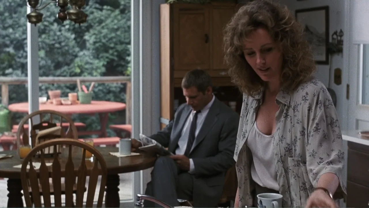 Presumed Innocent (1990) movie still: medium — A suburban dining area features a round wooden table, a wooden hutch, and a sliding glass door. A…