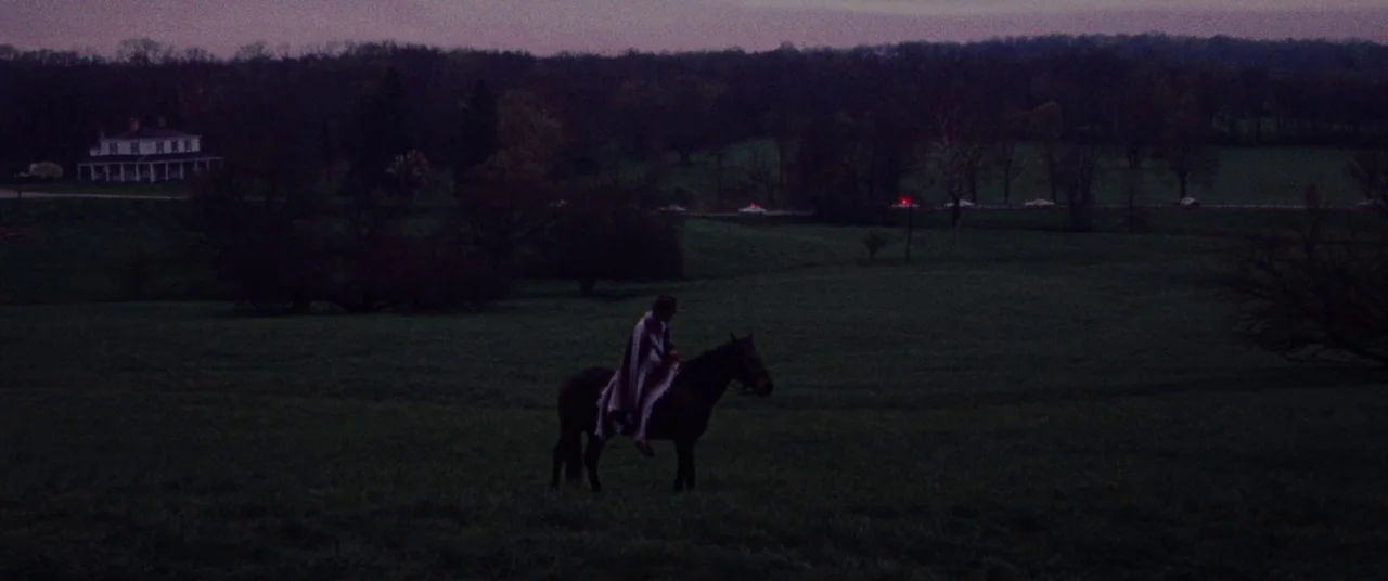 The Old Man & The Gun (2018) movie still: wide — A vast, dark field at dusk features a lone rider on a horse. A distant farmhouse and a line of…