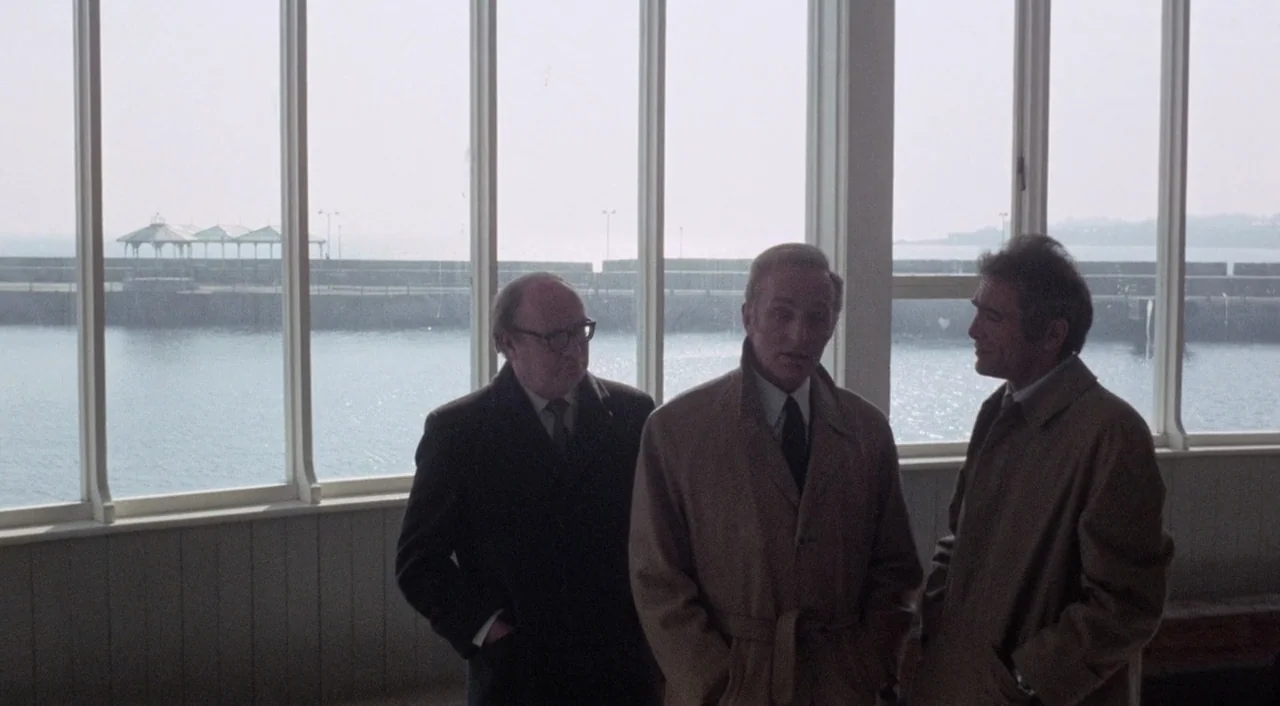 The Iguana with the Tongue of Fire (1971) movie still: medium — An interior space with large glass windows overlooking a concrete pier and calm…