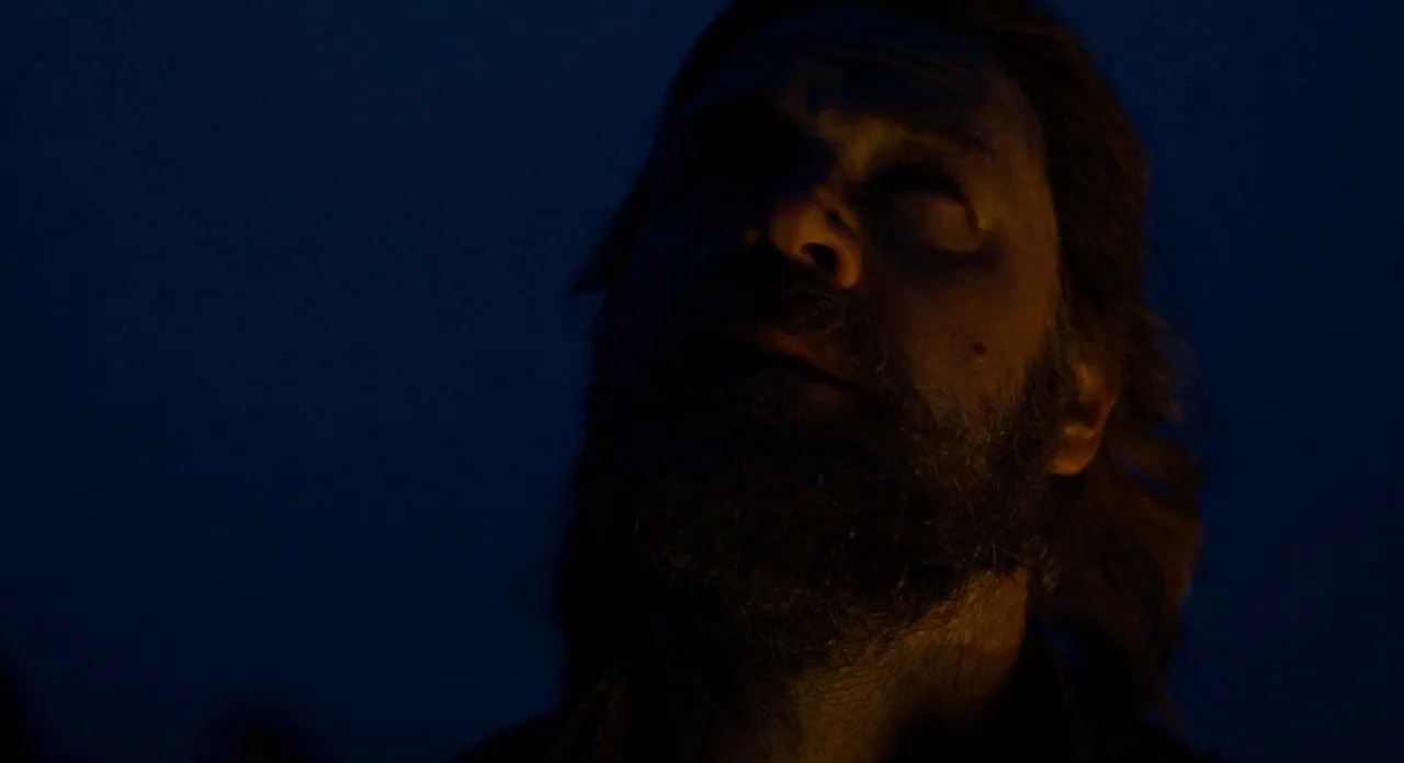 Noah (2014) movie still: closeup — A dark outdoor setting at night surrounds a man. He stands still while illuminated by a low-angled, warm light…