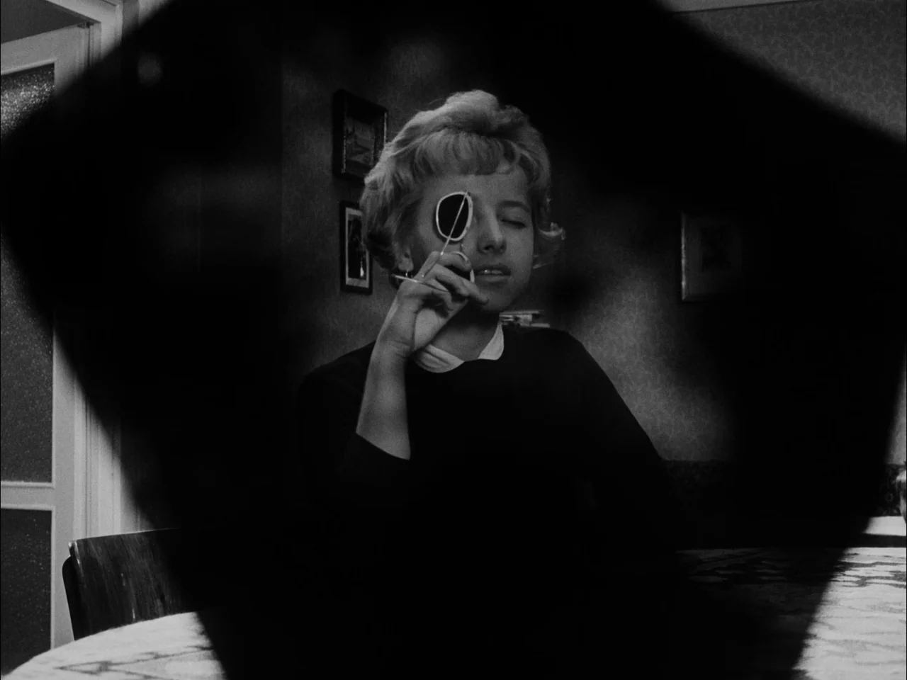 The Sun In A Net (1963) movie still: medium — A dark, dimly lit room is framed by an abstract geometric shape in shadow. A woman sits at a table and…