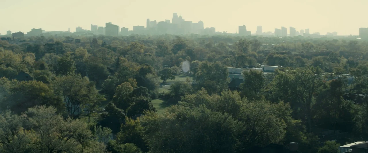 Don’t Breathe 2 (2021) movie still: establishing — A dense urban skyline rises above a suburban landscape covered in mature green trees. The distant…