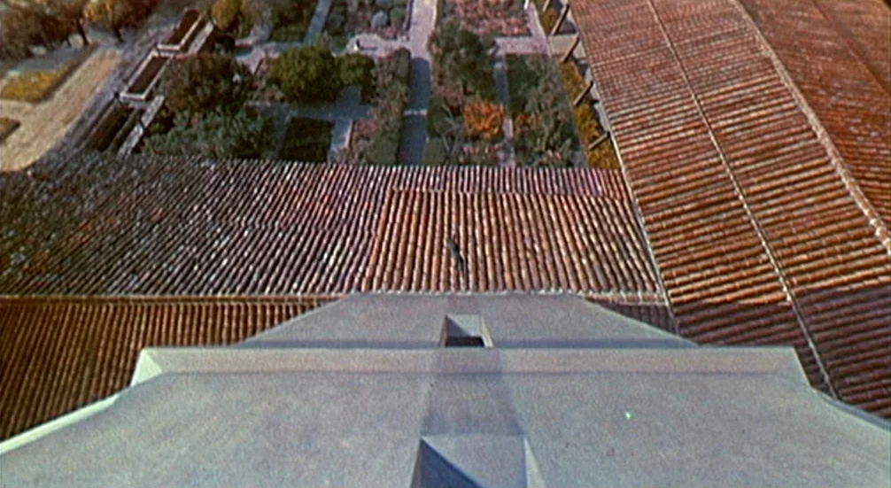 Vertigo (1958) movie still: establishing — An extreme top-down view shows the steep terracotta roof of a bell tower. A small figure is positioned on…