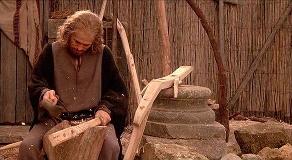 The Last Temptation Of Christ (1988) movie still: medium — An outdoor workspace is enclosed by a reed-mat fence and contains weathered stone…