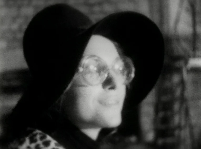 Cuadecuc, Vampir (1971) movie still: closeup — A close-up shot of a person in a dimly lit indoor space. The subject wears a dark wide-brimmed hat…