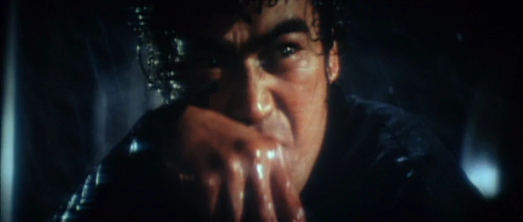 True Romance (1993) movie still: closeup — A man stands outdoors in darkness during a heavy rainstorm at night. His face is illuminated by a sharp…