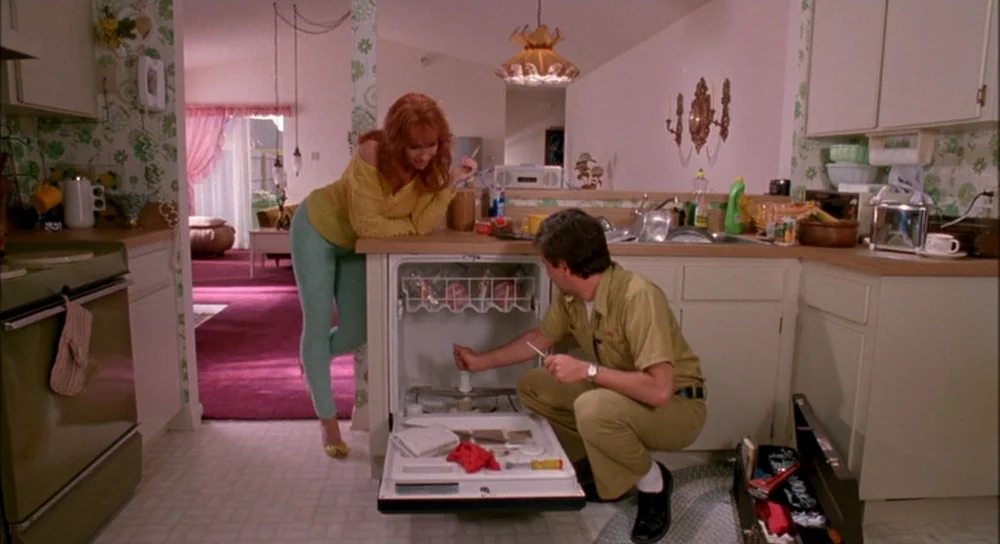 Edward Scissorhands (1990) movie still: medium — A 1980s suburban home features floral wallpaper and a pink-carpeted living room beyond. A…
