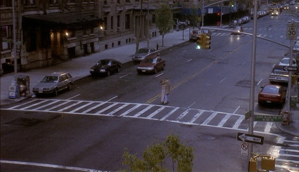 The Mirror Has Two Faces (1996) movie still: wide — A quiet New York City intersection at night features a wide asphalt crosswalk. A couple stands…