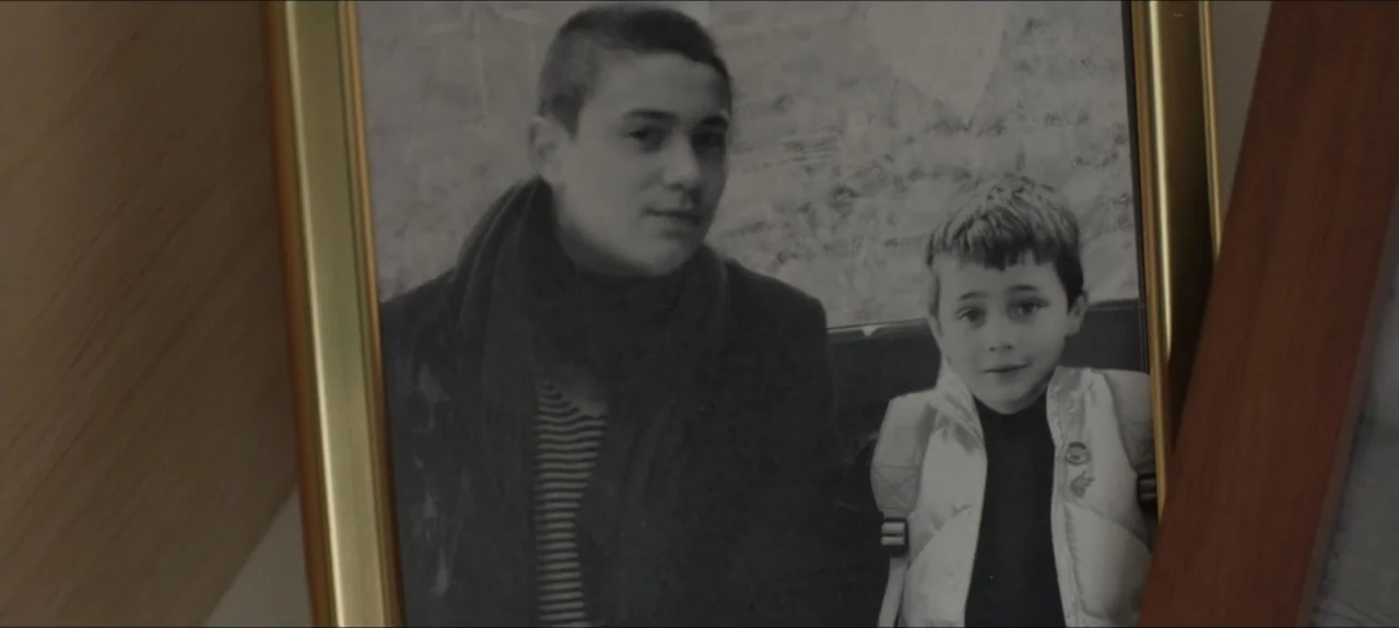 Containment (2015) movie still: closeup — A framed black and white photograph captures a portrait of a teenager and child. The two subjects stand…