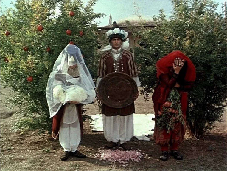 Ashik Kerib (1988) movie still: fullbody — Three people in traditional garments stand in an orchard filled with pomegranate trees. The central man…
