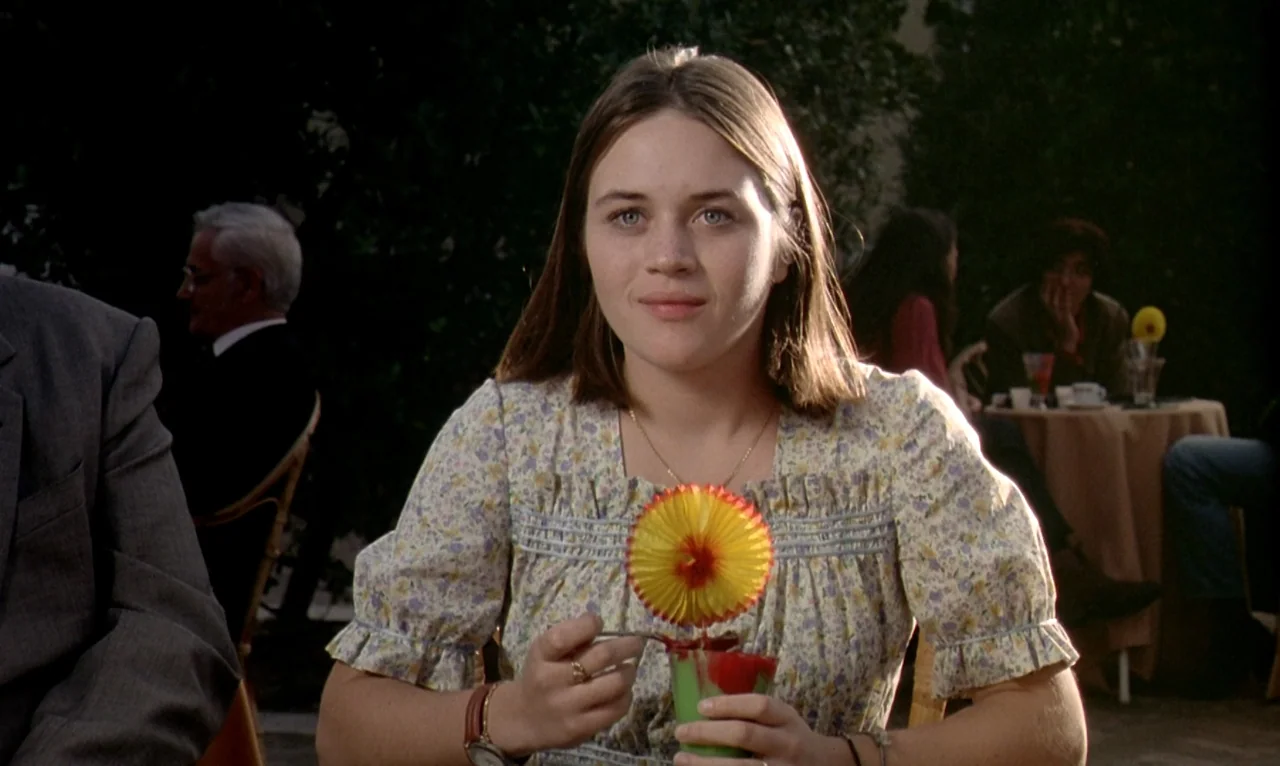 Dellamorte Dellamore (1994) movie still: medium — An outdoor seating area features a woman at a table with other patrons nearby. She sits at a table…