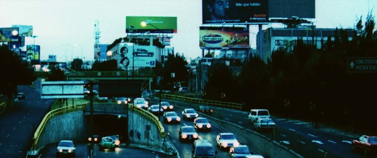 Man on Fire (2004) movie still: wide — A multi-lane highway at dusk features a dark tunnel entrance and large illuminated billboards. Multiple cars…