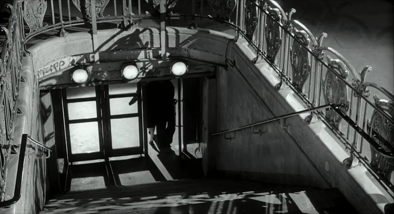 The Bohemian Life (1945) movie still: wide — A stone subway staircase descends into a dark underground portal at night. A lone figure moves through…