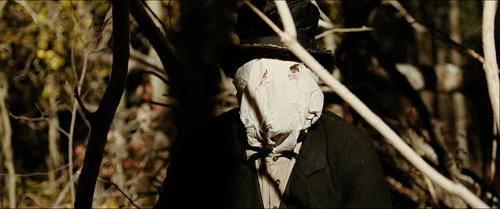 The Assassination Of Jesse James By The Coward Robert Ford (2007) movie still: closeup — A figure stands in a dense thicket of trees and branches…