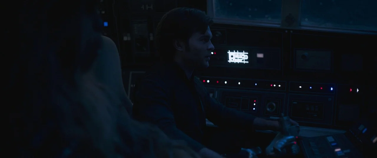Solo: A Star Wars Story (2018) movie still: medium — A dimly lit flight deck features arrays of dark control panels with small glowing lights. A man…