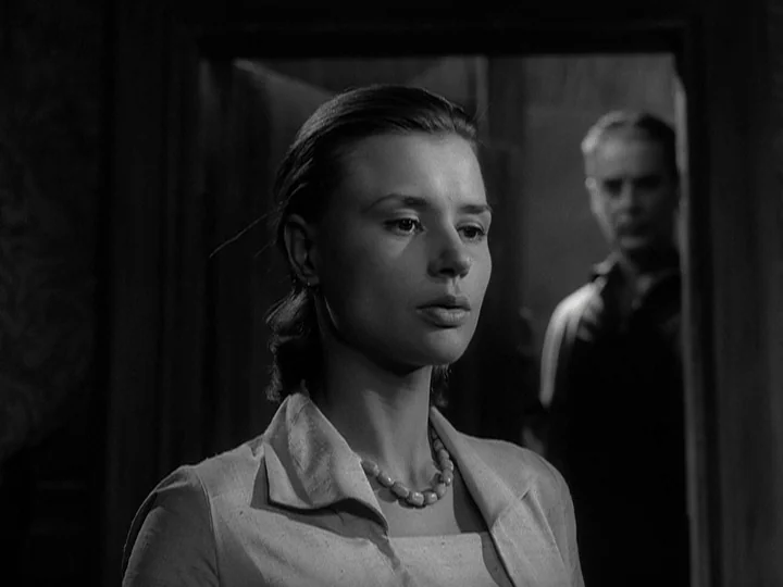 Through A Glass Darkly (1961) movie still: medium — A dark interior scene shows a woman positioned in the foreground of a doorway. A man stands…