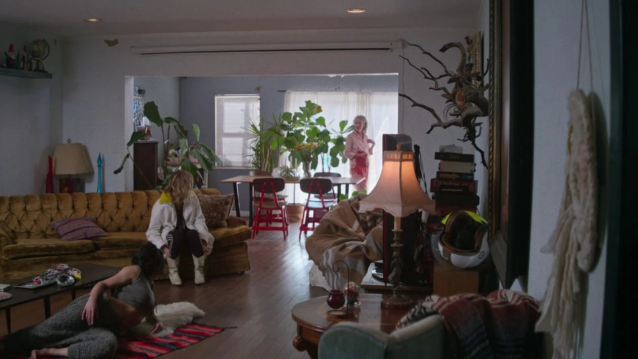She Dies Tomorrow (2020) movie still: wide — A cluttered living room features vintage furniture, numerous potted plants, and diverse decorative…