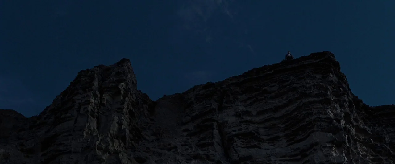 Far from the Madding Crowd (2015) movie still: wide — A dark, rocky cliff face looms against a clear midnight sky. A lone person sits at the very…