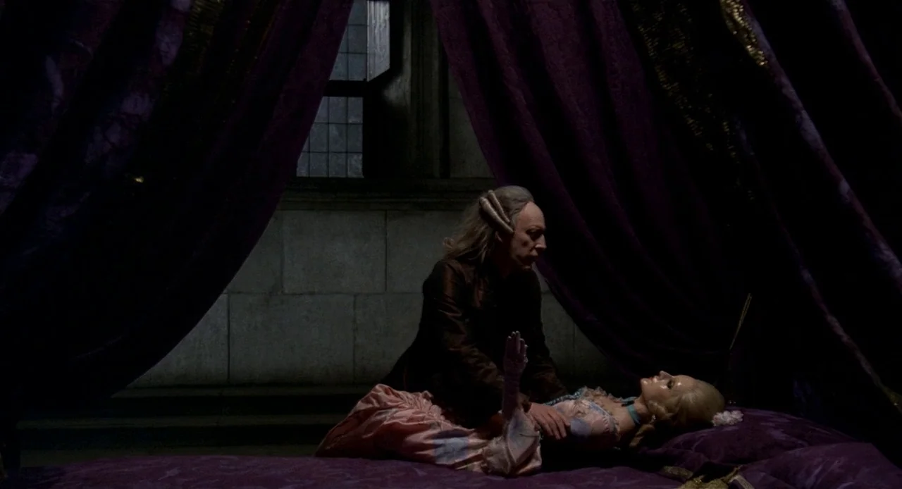 Fellini’s Casanova (1976) movie still: medium — A dimly lit room features a large bed draped with heavy purple fabric curtains. A man in a dark…