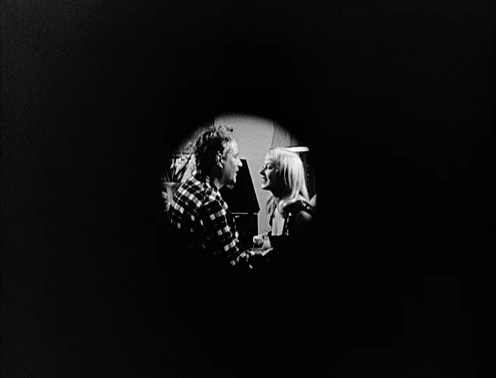 Nights of Cabiria (1957) movie still: medium — A dark indoor space viewed through a circular aperture like a peephole. A man in a flannel shirt and…