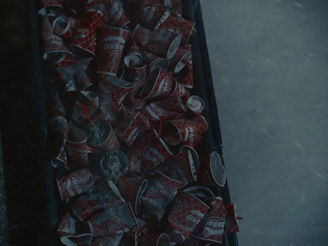 I’m Thinking of Ending Things (2020) movie still: closeup — A heap of discarded red and white paper drink cups fills a metal container. The cups are…