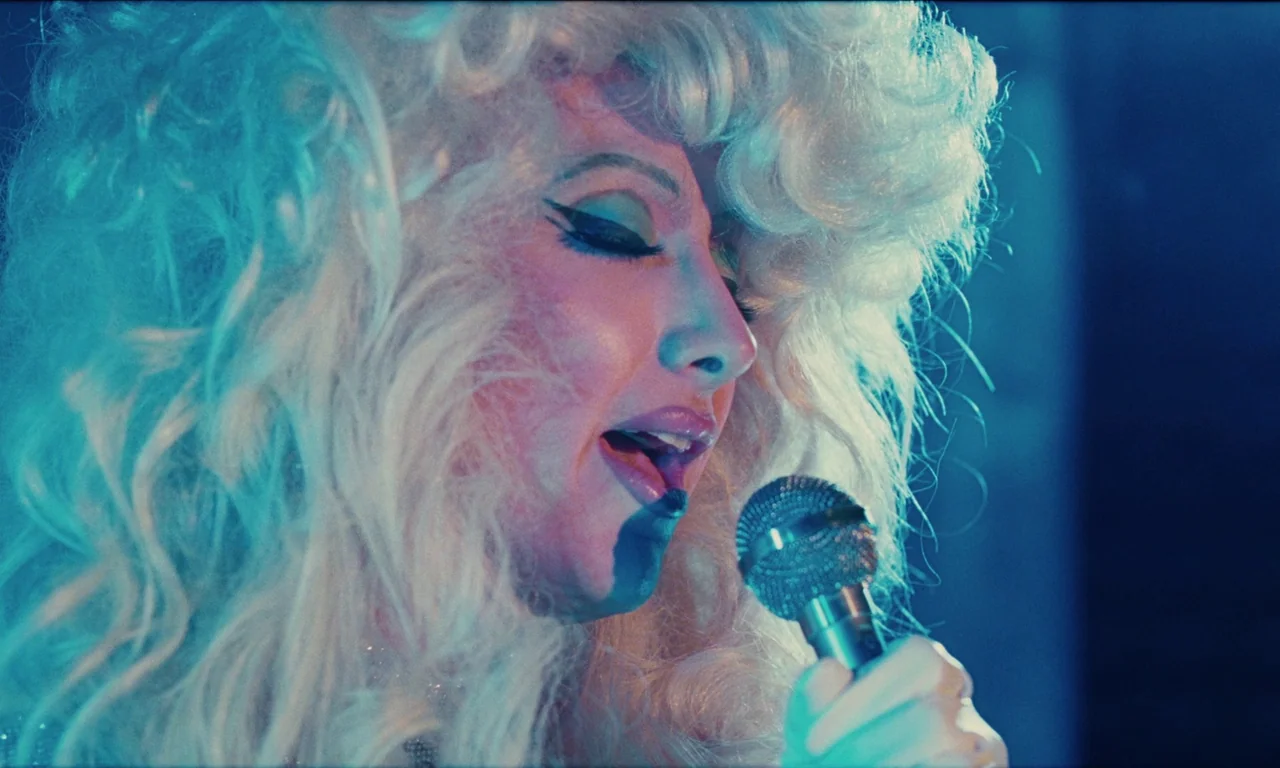 National Anthem (2023) movie still: closeup — A performer stands on a darkened stage illuminated by intense blue lighting. She sings with eyes…