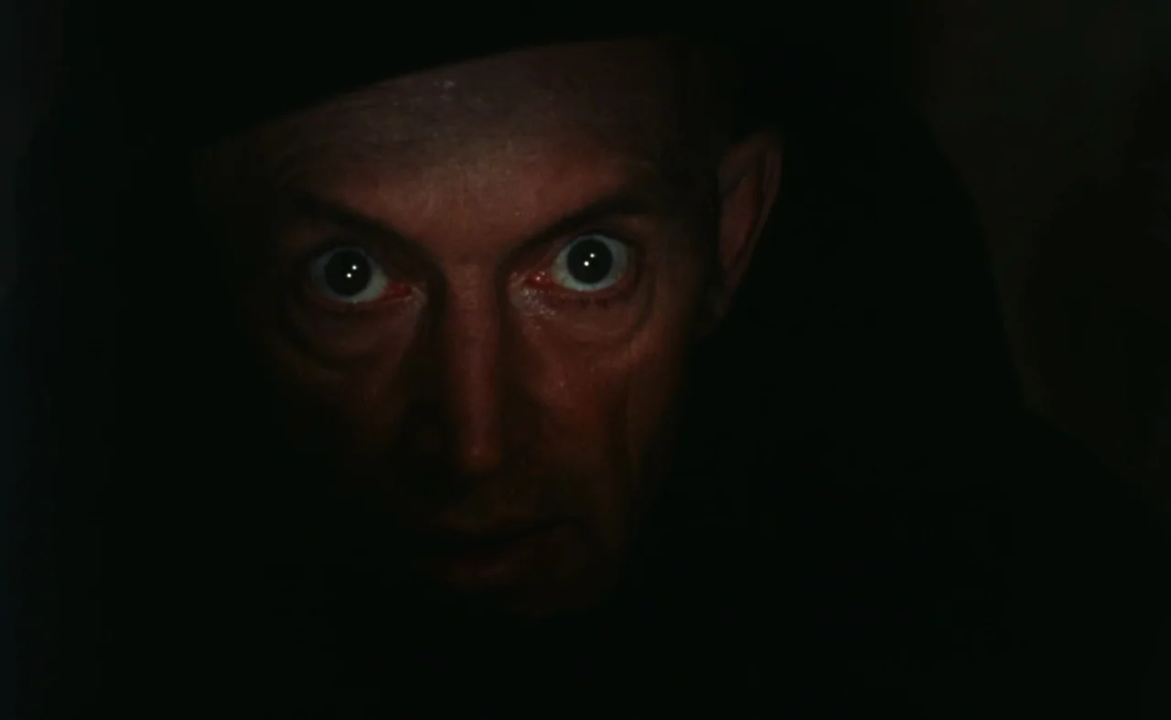 The Pit and The Pendulum (1991) movie still: closeup — A man's face emerges from total darkness into a soft light source. He stares directly forward…