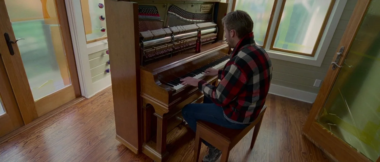 Song to Song (2017) movie still: medium — An interior space features wood flooring and large windows with frosted glass segments. A man sits at a…