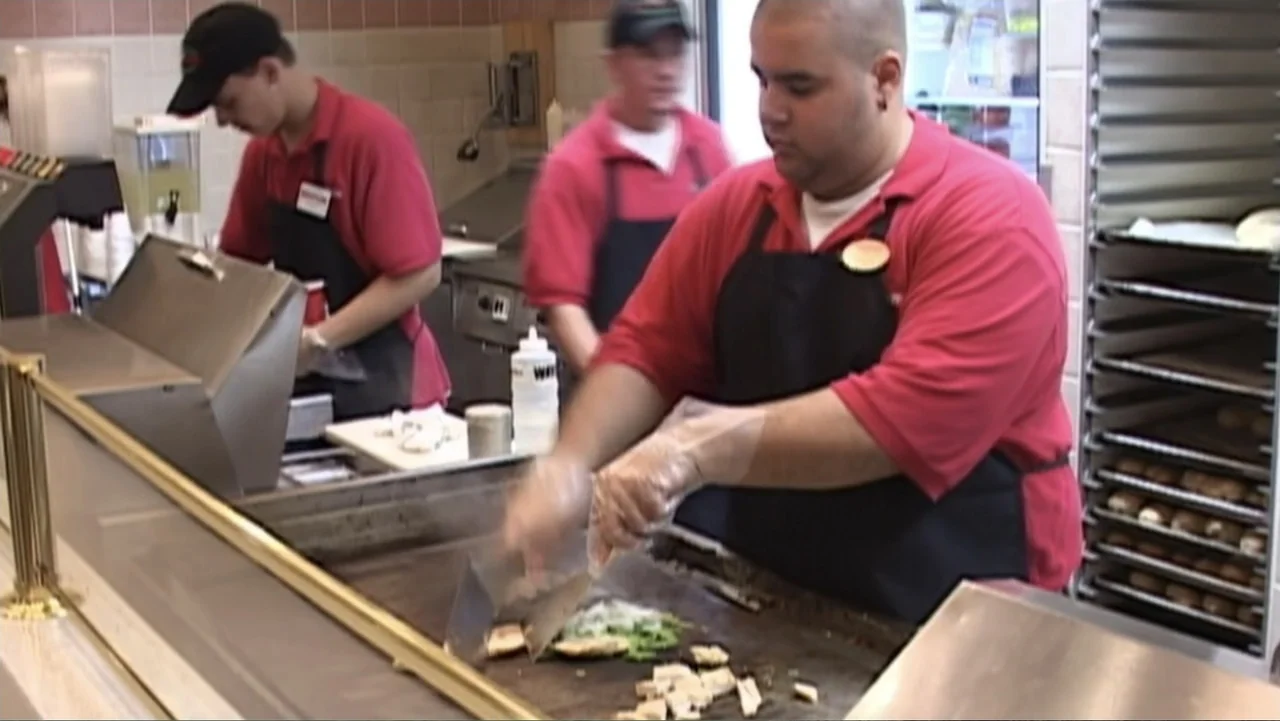 Super Size Me (2004) movie still: medium — A stainless steel commercial food preparation area features a large, busy flat-top grill. A young man in…