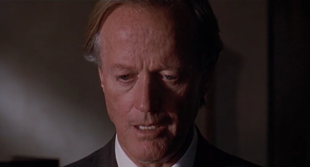 The Heart Is Deceitful Above All Things (2004) movie still: closeup — A man stands in a dimly lit indoor space with neutral-toned walls behind him.…