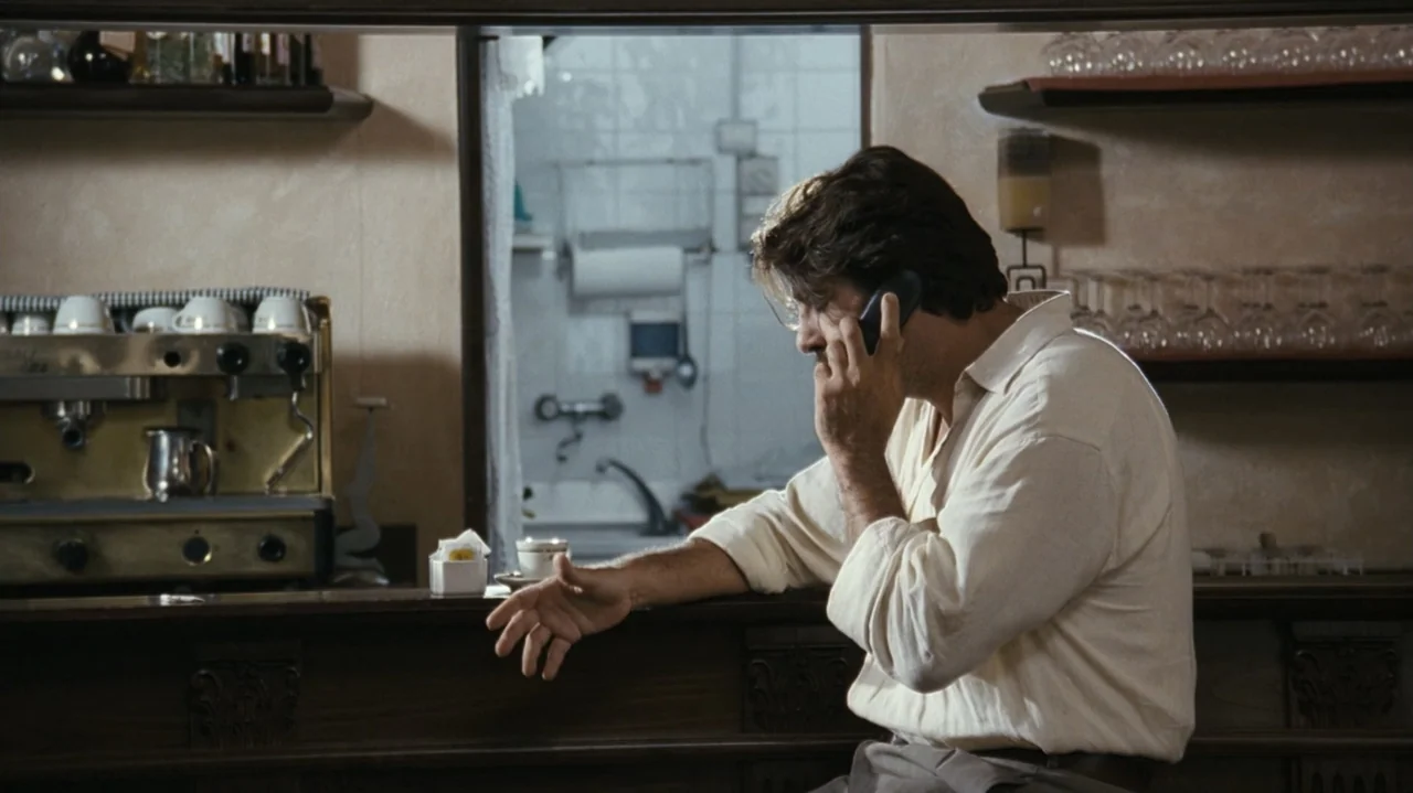 Shadows in the Sun (2005) movie still: medium — An interior cafe space features a wooden bar counter and shelves displaying glassware and espresso…