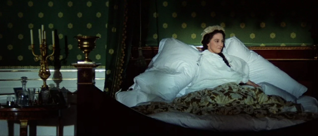 Ludwig (1973) movie still: medium — An 1800s bedroom features dark green wallpaper with repeating gold floral patterns. A woman in a white nightgown…