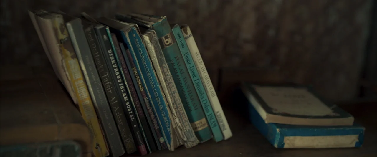 The Unholy (2022) movie still: closeup — A row of worn, vintage books with colored spines sits upright on a shelf. A separate, horizontal book lies…